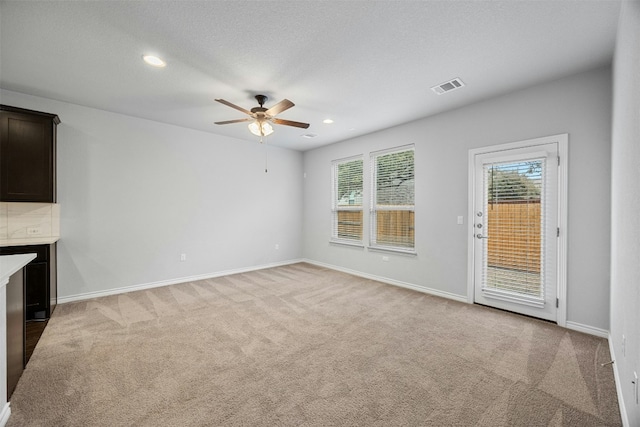 unfurnished living room featuring light colored carpet, visible vents, plenty of natural light, and baseboards