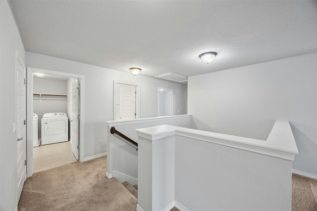 hallway featuring washing machine and dryer, light carpet, a textured ceiling, and an upstairs landing