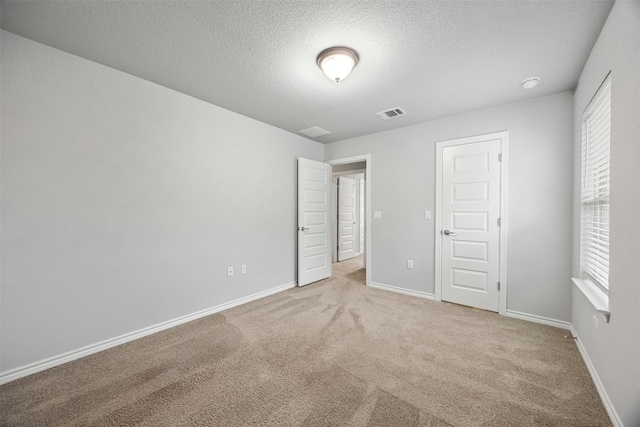 unfurnished bedroom featuring light colored carpet, visible vents, baseboards, and a textured ceiling