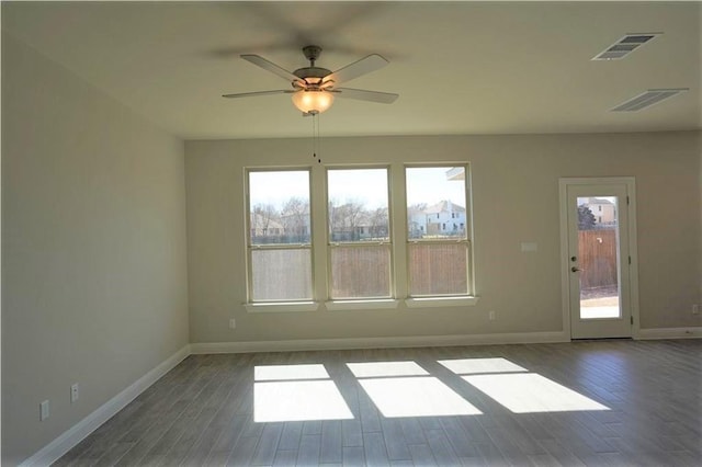 spare room featuring a ceiling fan, visible vents, baseboards, and wood finished floors