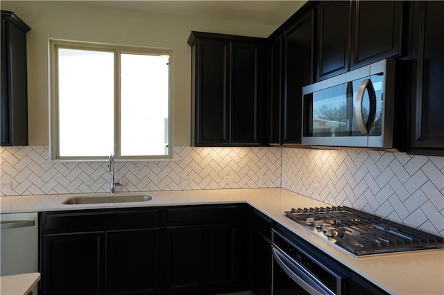 kitchen featuring stainless steel appliances, dark cabinetry, a sink, and light countertops