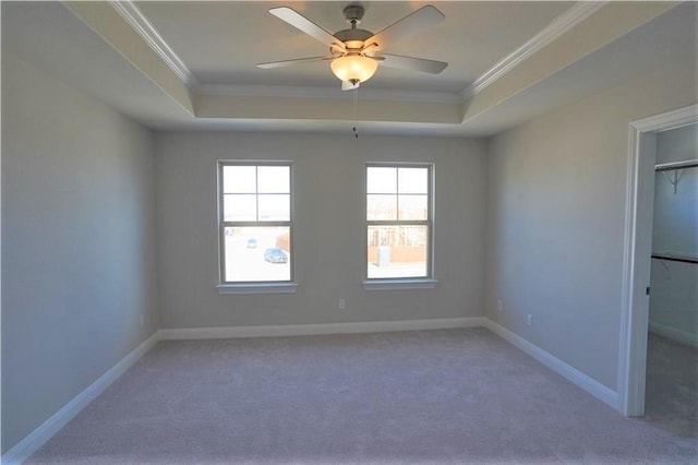 carpeted empty room featuring ceiling fan, baseboards, a raised ceiling, and crown molding