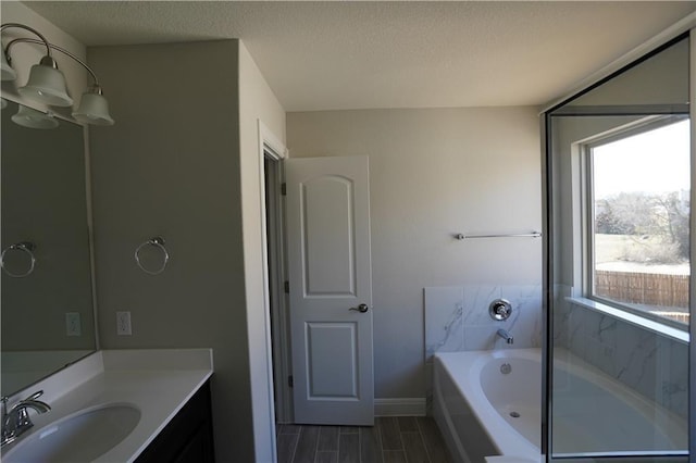 full bath featuring a textured ceiling, a garden tub, wood finish floors, vanity, and baseboards