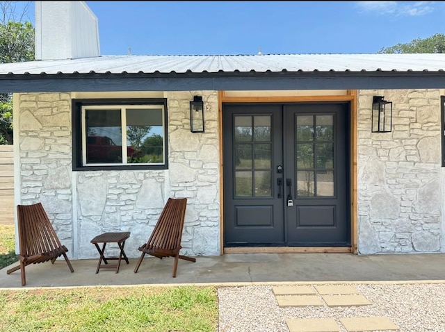 entrance to property with stone siding, french doors, and metal roof