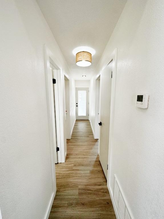 hallway with visible vents, baseboards, and wood finished floors