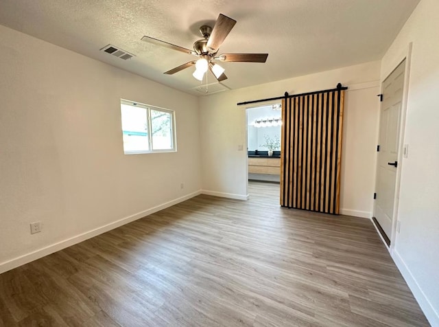 unfurnished room with baseboards, a barn door, visible vents, and wood finished floors