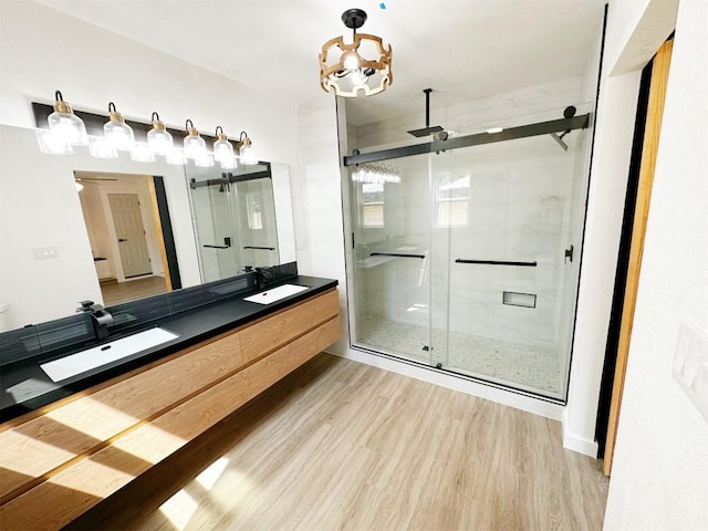 bathroom with a notable chandelier, a sink, wood finished floors, a shower stall, and double vanity