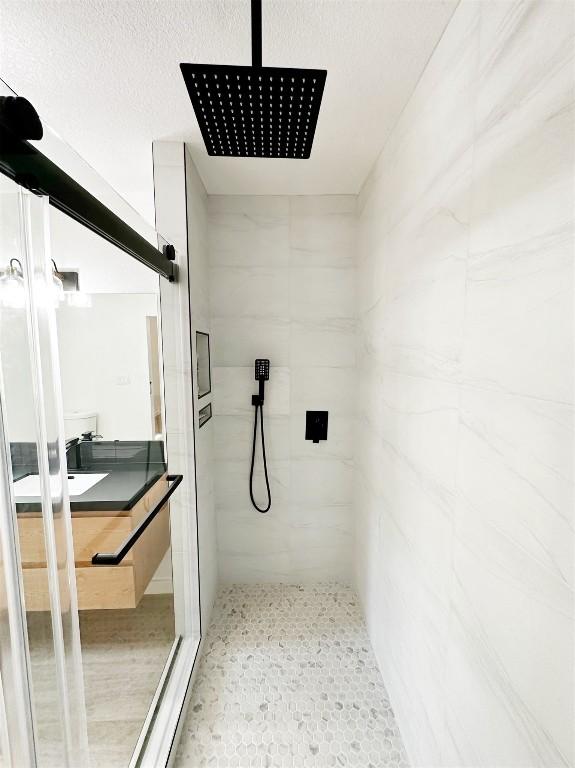 bathroom featuring a textured ceiling, tiled shower, and vanity