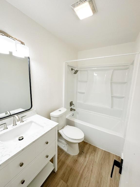 bathroom with visible vents, toilet, wood finished floors, vanity, and washtub / shower combination