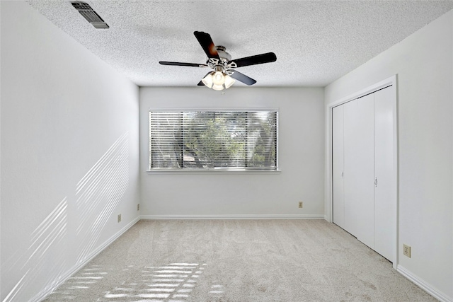 unfurnished bedroom with a textured ceiling, carpet flooring, visible vents, baseboards, and a ceiling fan