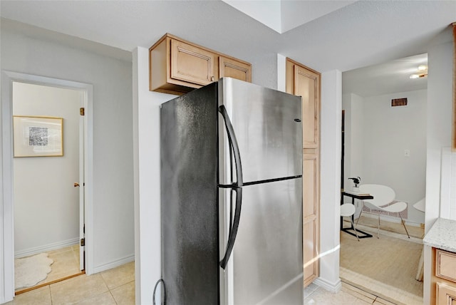 kitchen featuring light stone counters, light tile patterned floors, visible vents, freestanding refrigerator, and baseboards