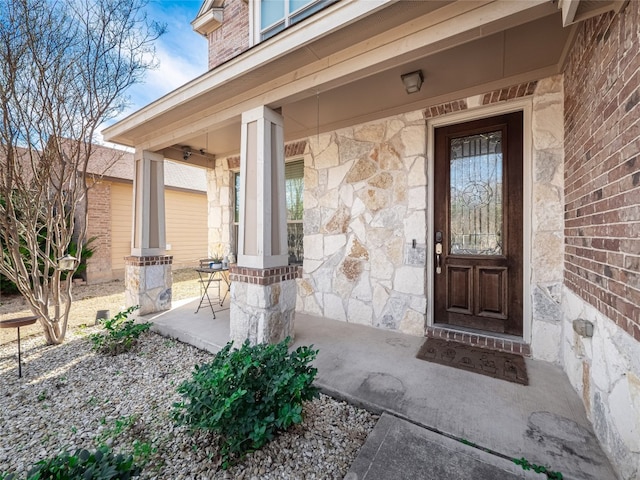 doorway to property with covered porch, stone siding, and brick siding