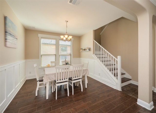 dining area with dark wood-type flooring, visible vents, stairs, wainscoting, and an inviting chandelier