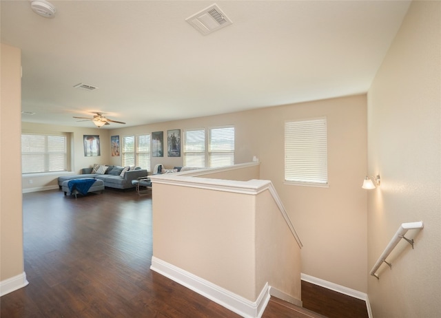 corridor featuring dark wood-style floors, baseboards, visible vents, and an upstairs landing