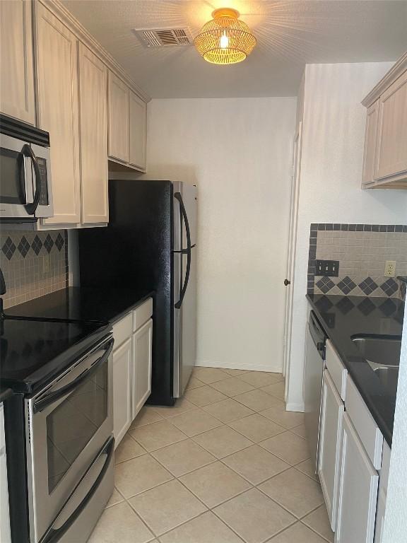 kitchen featuring stainless steel appliances, dark countertops, visible vents, and backsplash