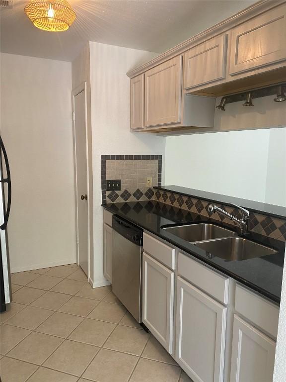 kitchen with light tile patterned floors, tasteful backsplash, dishwasher, dark countertops, and a sink