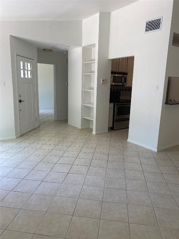 unfurnished room with built in features, light tile patterned floors, visible vents, vaulted ceiling, and baseboards