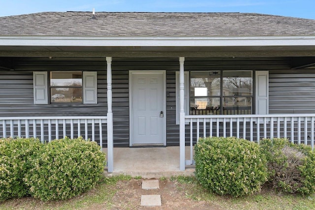 entrance to property with a porch and roof with shingles