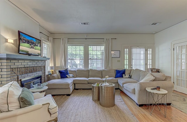 living area with a brick fireplace, light wood-style flooring, visible vents, and french doors