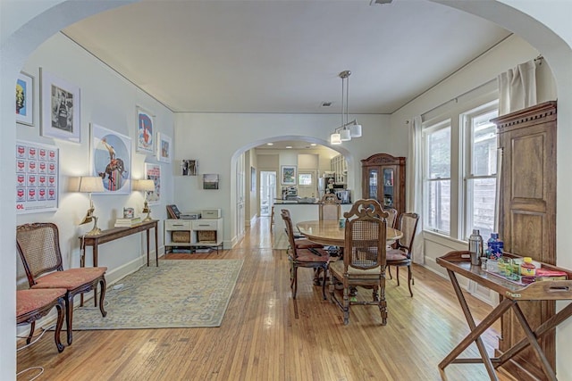 dining room with light wood-style flooring, arched walkways, and baseboards