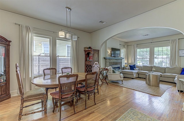 dining area with arched walkways, a brick fireplace, visible vents, and light wood-style flooring