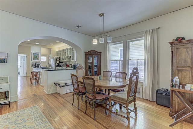 dining space featuring light wood finished floors, visible vents, and arched walkways