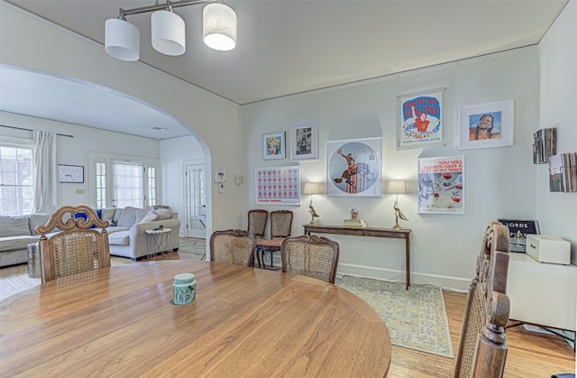 dining room with arched walkways, wood finished floors, and baseboards