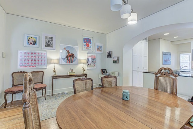 dining area with arched walkways, light wood-style flooring, and baseboards