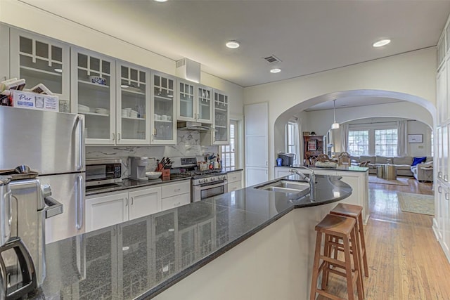 kitchen with arched walkways, light wood-style flooring, appliances with stainless steel finishes, open floor plan, and a sink