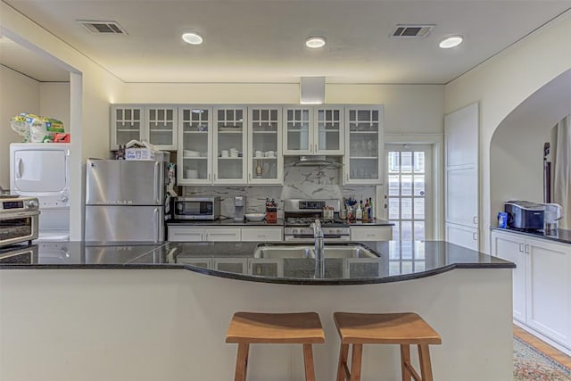 kitchen with appliances with stainless steel finishes, stacked washer and dryer, visible vents, and a breakfast bar area