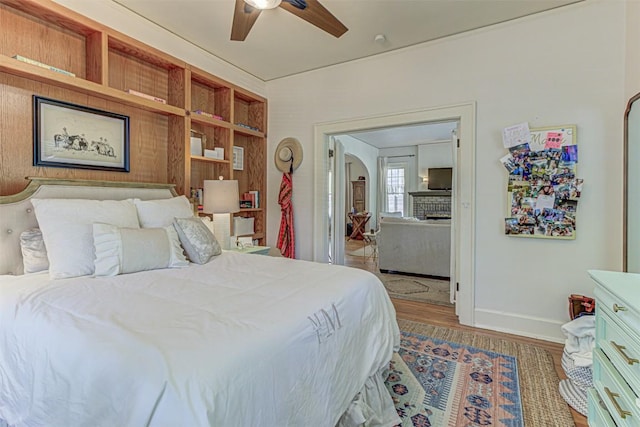 bedroom with arched walkways, wood finished floors, a ceiling fan, and baseboards