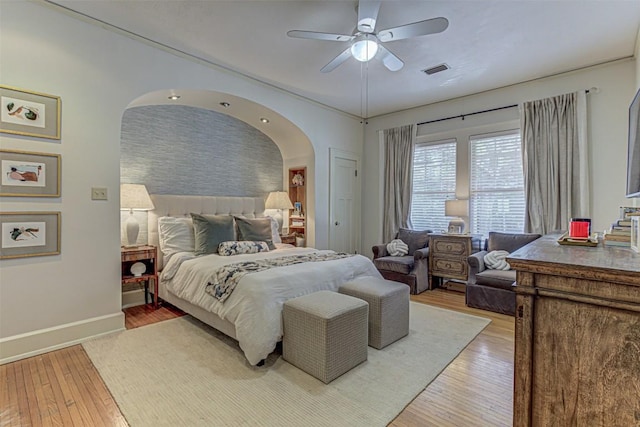 bedroom with arched walkways, light wood finished floors, visible vents, ceiling fan, and baseboards