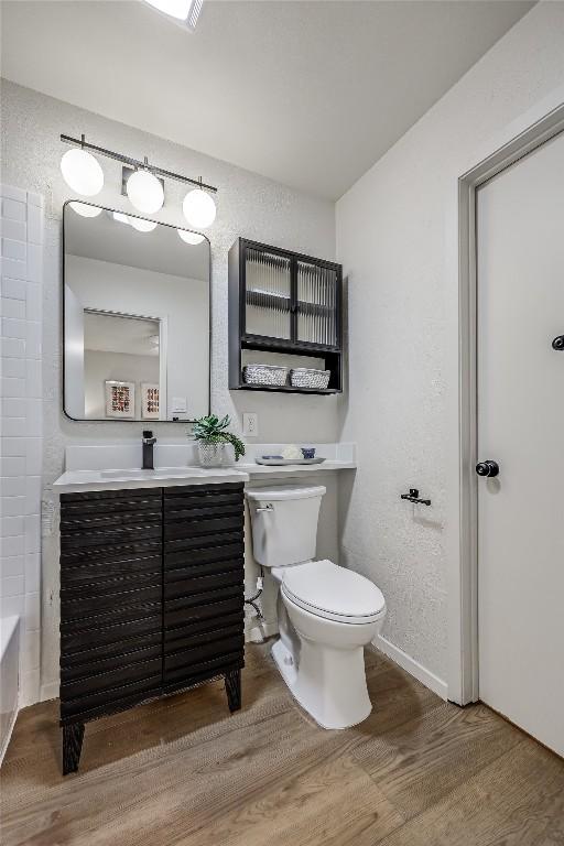 full bath with a textured wall, vanity, wood finished floors, and toilet