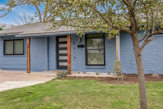 view of front of house with roof with shingles, a front lawn, and brick siding