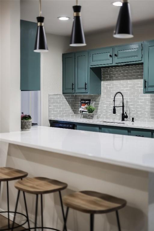 kitchen featuring a breakfast bar area, a sink, light countertops, backsplash, and decorative light fixtures