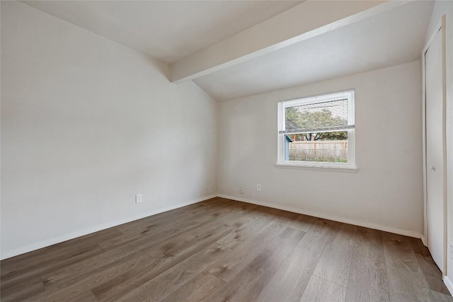 unfurnished room featuring vaulted ceiling with beams, wood finished floors, and baseboards