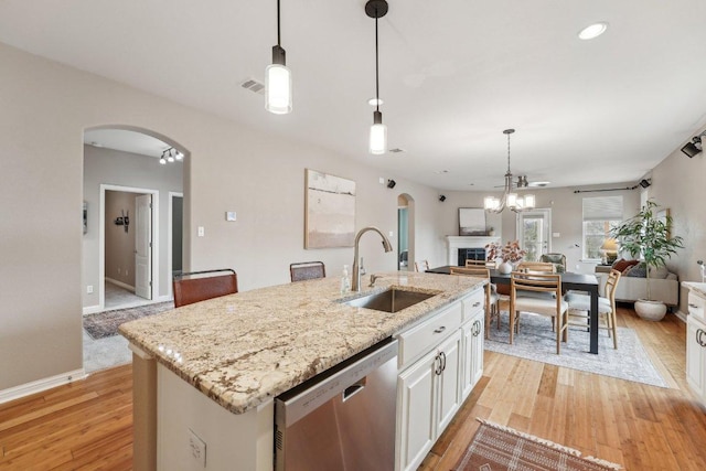 kitchen with a sink, arched walkways, open floor plan, and stainless steel dishwasher