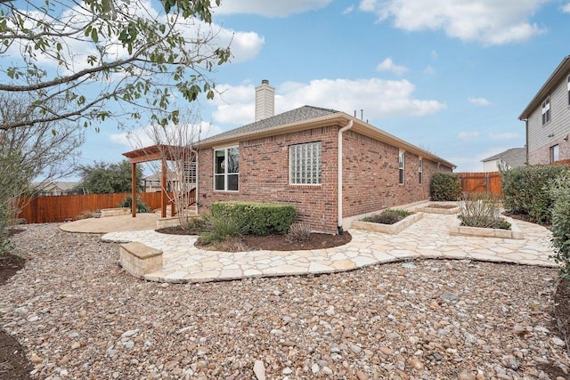 view of side of property featuring brick siding, a chimney, a patio area, and a fenced backyard