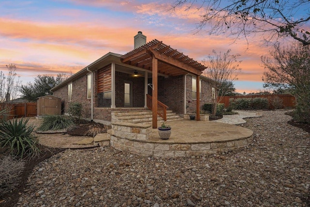 view of side of home featuring an outbuilding, brick siding, a chimney, a storage shed, and fence