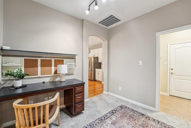 office space featuring light carpet, visible vents, arched walkways, baseboards, and track lighting