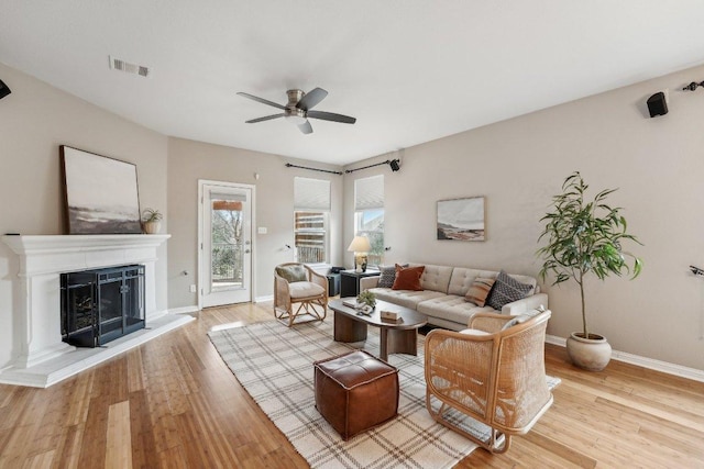 living area featuring a fireplace with raised hearth, wood finished floors, visible vents, and a ceiling fan