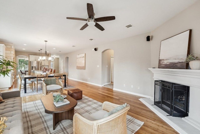 living room featuring light wood-type flooring, baseboards, visible vents, and a fireplace with raised hearth