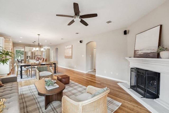 311 Limestone Trl, Austin, TX 78737 - living room featuring arched walkways, a ceiling fan, light wood-style floors, a fireplace with raised hearth, and baseboards