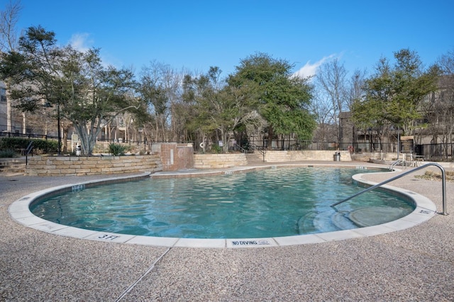 community pool with a patio area and fence