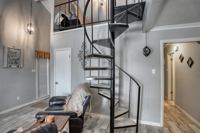 stairway with crown molding, a high ceiling, baseboards, and wood finished floors