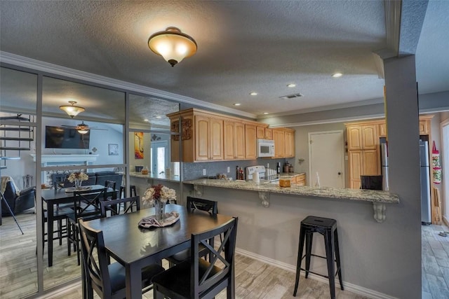 kitchen featuring visible vents, range, white microwave, ornamental molding, and freestanding refrigerator