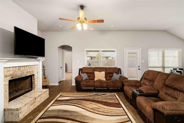 living area featuring arched walkways, a brick fireplace, plenty of natural light, and wood finished floors