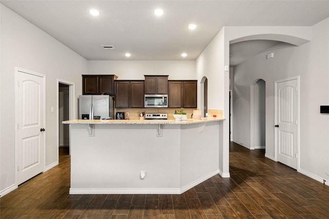 903 Mclaury Cv, Killeen, TX 76542 - kitchen with stainless steel appliances, arched walkways, light stone counters, dark brown cabinetry, and a kitchen bar