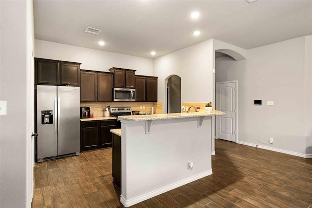 903 Mclaury Cv, Killeen, TX 76542 - kitchen featuring stainless steel appliances, arched walkways, dark brown cabinets, a breakfast bar area, and dark wood finished floors