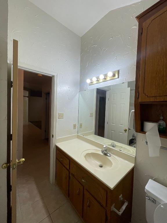 bathroom with lofted ceiling, vanity, toilet, and tile patterned floors